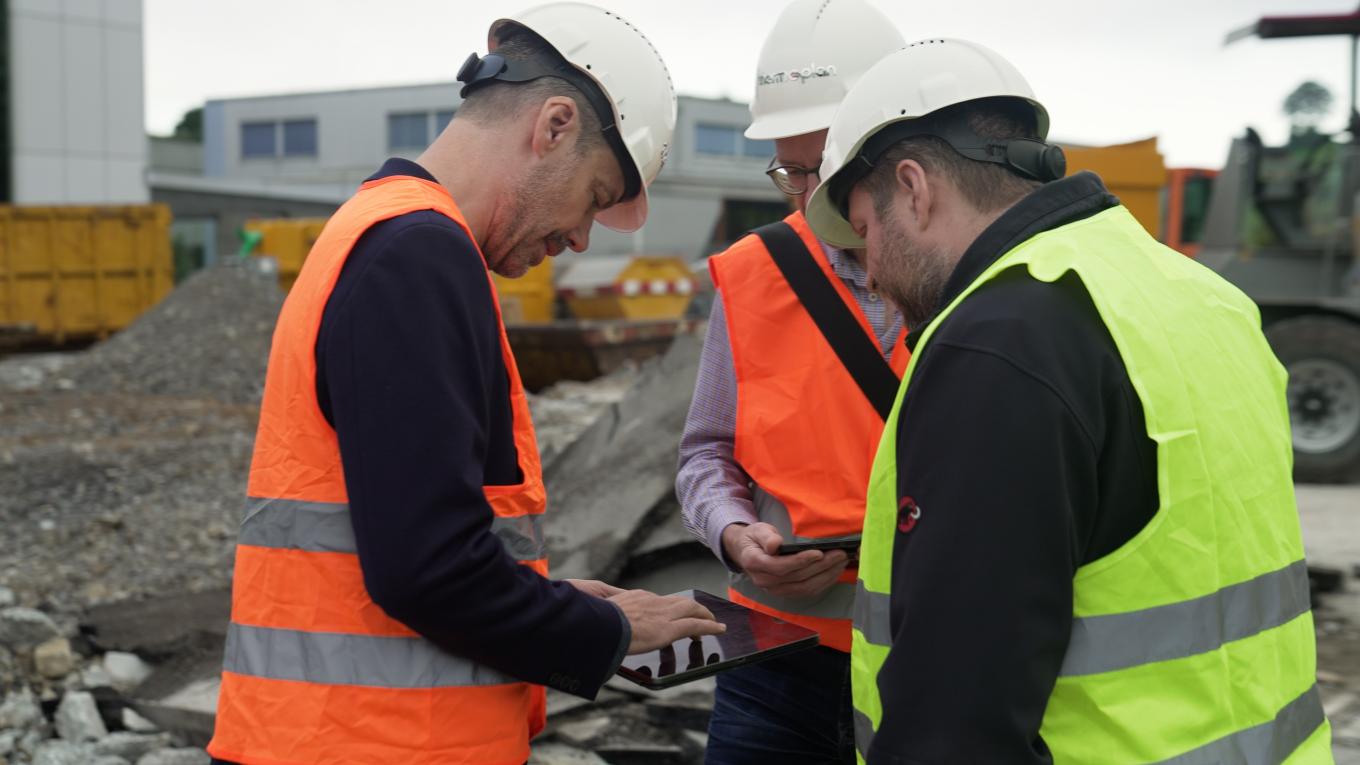 drei Personen auf der Baustelle die gemeinsam auf ein Tablet schauen