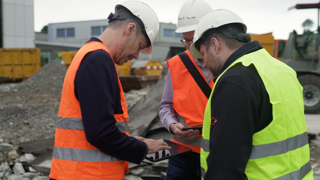 drei Personen auf der Baustelle die gemeinsam auf ein Tablet schauen